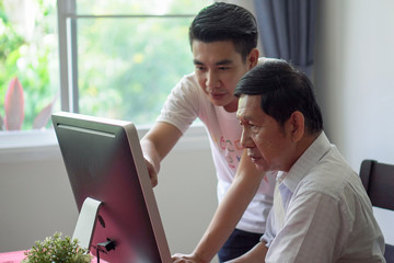 Grandson teaching grandfather how to Using computer and technology in home . young Teacher help...