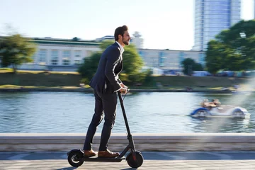Foto op Plexiglas Young business man in a suit riding an electric scooter on a business meeting. © opolja