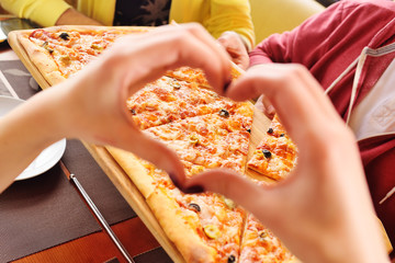 hands folded in the shape of a heart close-up on the background of fresh hot pizza