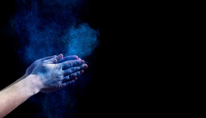 Hands clapping with blue holi powder on black