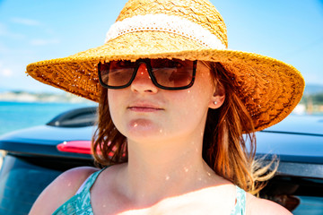 Happy woman in a hat and a summer car on the sunny sandy beach.