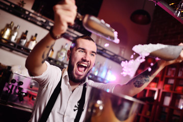 a handsome bearded bartender in a white shirt pours ice for cocktails and screams happily against...