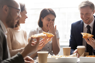 Happy asian worker laugh hold slice eating pizza with colleagues