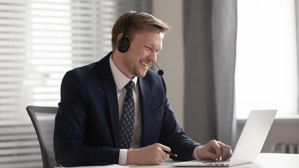 Smiling businessman wear wireless headset video calling looking at laptop
