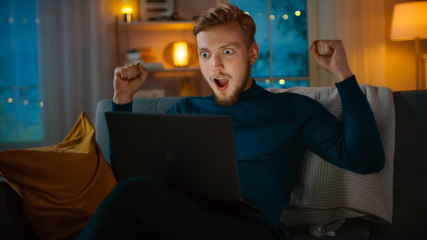 In the Evening: Portrait of Handsome Young Man Using Laptop while Sitting on a Couch at Home,...
