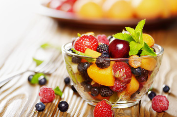 Assorted fruits in glass bowl on kitchen wooden table with fork aside