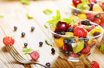 Assorted fruits in glass bowl on kitchen wooden table with fork aside