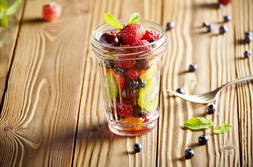 Assorted berries in mason jar on kitchen wooden table with fork aside