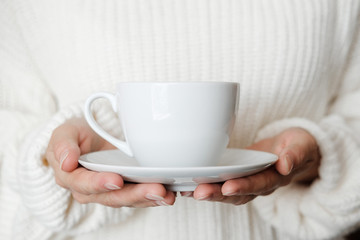 Woman in white knitted sweater holding cup of coffee. Female hands with cup of tea. Close up