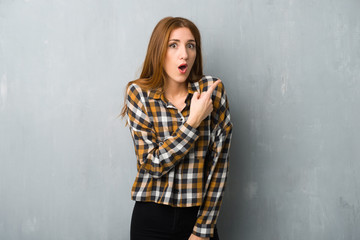 Naklejka premium Young redhead girl over grunge wall surprised and pointing side