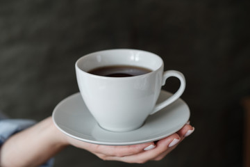 Woman holding cup of coffee. Female hands with cup of black tea on dark background. Close up