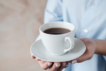 Woman holding cup of coffee. Female hands with cup of black tea on beige background. Close up