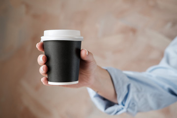 Woman in blue blouse holding black cup of coffee. Female hands with cup of black tea on beige background. Close up