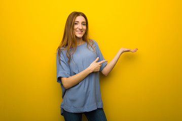 Young redhead girl over yellow wall background holding copyspace imaginary on the palm to insert an...