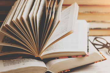 An open book with glasses on a wooden table against the background of a set of books, vintage toning. Literature, learning concept