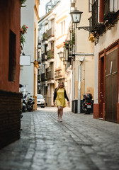 Fototapeta na wymiar Summer outdoor portrait of young beautiful woman in yellow dress. Cheerful blond girl walking between old stone houses. Enjoying vacation in Portugal. Travel and active lifestyle concept