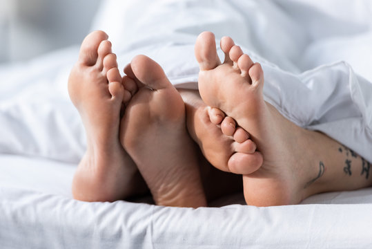 partial view of two barefoot lesbians lying under blanket