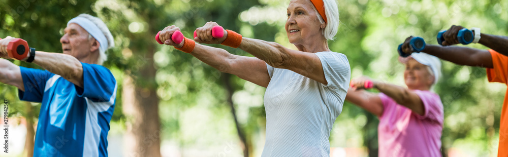 Wall mural panoramic shot of senior pensioners exercising with dumbbells in park