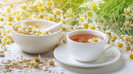 Rural still-life - cup of brewed chamomile tea on the background of a bouquet of daisies, closeup