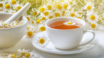Rural still-life - cup of brewed chamomile tea on the background of a bouquet of daisies, closeup