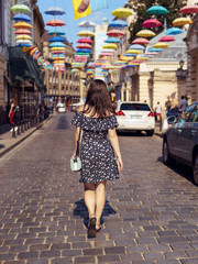 Young woman in stylish dress walking down the street alone and looking around. 