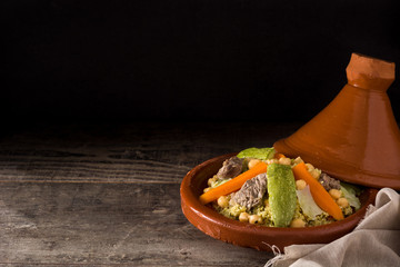 Traditional tajine with vegetables, chickpeas, meat and couscous on wooden table. Copyspace