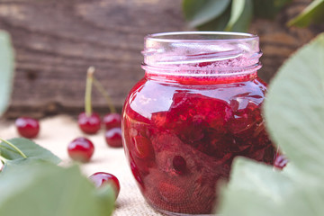 Fresh cherry jelly with fruit on a wooden background near the berries and green leaves.
