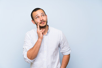 Colombian man over isolated blue wall thinking an idea while looking up