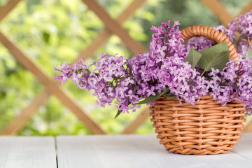 Basket with a bouquet of lilac flowers on a white wooden table in the summerhouse in the garden
