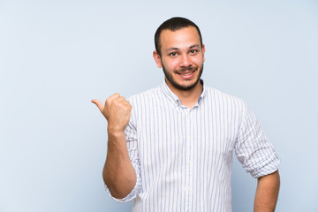 Colombian man over isolated blue wall pointing to the side to present a product