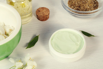 Jar of cream made from natural plant ingredients, oils and herbs, jasmine flowers, mortar and pestle on a white wooden background - preparation of organic cosmetics concept