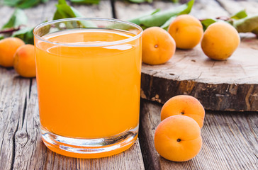 Fresh apricot juice with apricots and a branch with green leaves on the background of old boards.