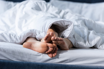 partial view of two barefoot lesbians lying under blanket
