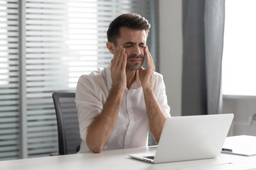 Stressed frustrated businessman suffer from strong headache attack at workplace
