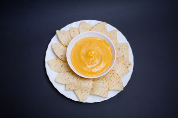 Queso chedar vegano con nachos para mojar sobre fondo negro.