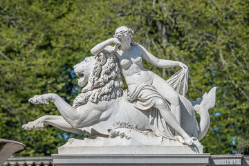 Fototapeta premium Old statue of sensual renaissance era woman laying on big lion in park, Potsdam, Germany, details, closeup