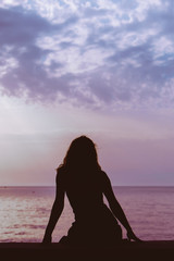 Fototapeta premium woman silhouette sitting on the beach looking at sunset over the sea