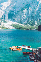 view of wooden house on water with pier and boats lake in dolomites mountains
