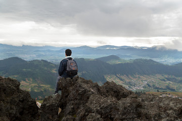 young man sitting on top of a mountain looking towards the mountains and landscape- general shot