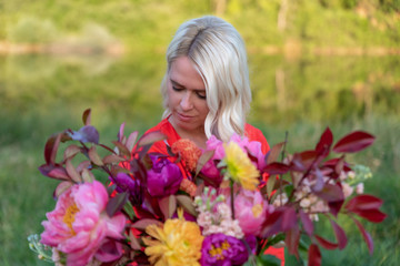 Naklejka premium Beautiful young woman with flowers in the field and a lake as a background