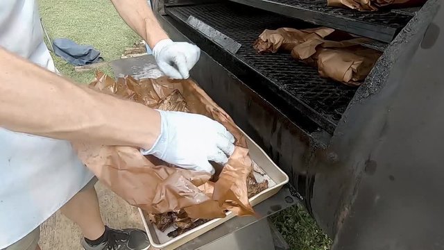 Person unwraps rack of pork ribs taken from rack of meat smoker