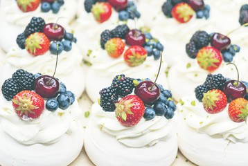 Pavlov cakes with fresh berries and cream. Lie in rows on a baking sheet in the confectionery shop.