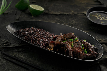  Korean-style bbq beef with black rice on a black wooden table.