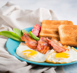 Fried eggs from two eggs with bacon, toast and spinach on a blue plate. Traditional English breakfast. Traditional Irish breakfast.