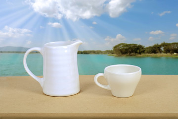 White coffee cup and jar on wood table with nature background.