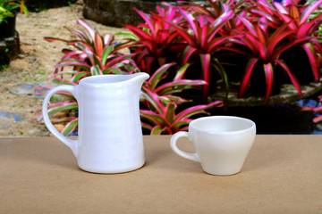 White coffee cup and jar on wood table with nature background.