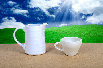 White coffee cup and jar on wood table with nature background.