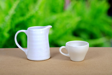 White coffee cup and jar on wood table with nature background.