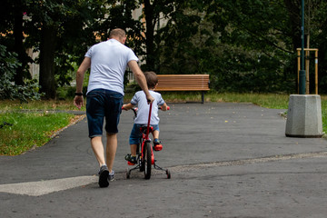 Father teaches a child to ride a bike. Spending time with your child. Father and son. The boy makes an attempt to ride a bike while his father supports him