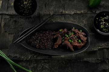 Delicious sticky Asian beef meat in black pepper sauce with black rice on a rustic wooden black table. Directly above top view shot.